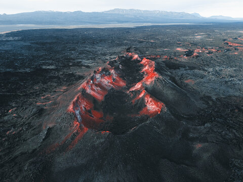 Aerial view of a volcano's dark slopes slashed with veins of fiery red, contrasting against the stark landscape, Highlands, Iceland.