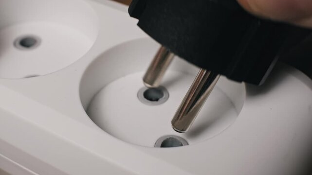 Close-up of a male hand unplugging a black Schuko power plug from a white dual socket extension cord. Disconnecting the appliance stops current flow for safety and energy saving.
