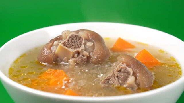 A bowl of hearty soup with meat and vegetables against a green background