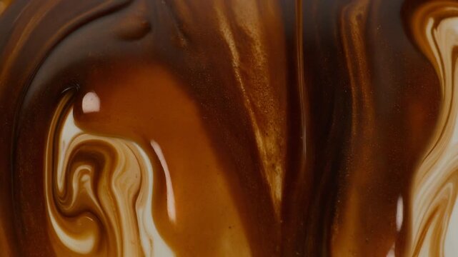 Decadent thick brown coffee mocha or chocolate dessert sauce swirling into white creamy milk creating a vibrant liquid marbling effect