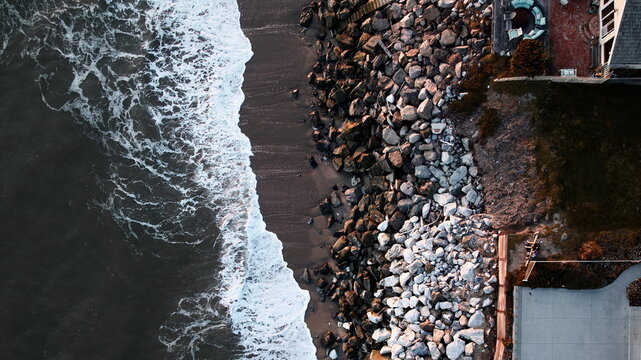 Aerial view of the dramatic contrast of the dark, swirling ocean against the rugged coastline, with homes perched along the bluffs, Santa Cruz, California, United States.