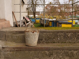 Naklejka premium Old galvanized metal bucket with rust standing on concrete steps in a yard.