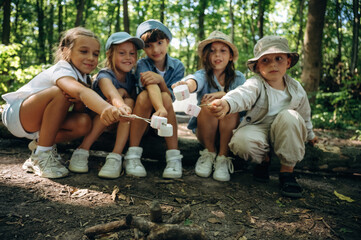 Fototapeta premium Tasty marshmallow are on sticks in hands. Group of children in the forest on a hike