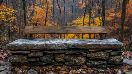 Weathered wooden bench with stone base sits in vibrant autumn forest, bathed in warm glow of fall foliage and fallen leaves, offering serene resting spot amidst nature's colorful display.