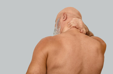Neck pain in naked bald man on gray. Upper half of male body naked. Suffers from neck pain. Treating.
