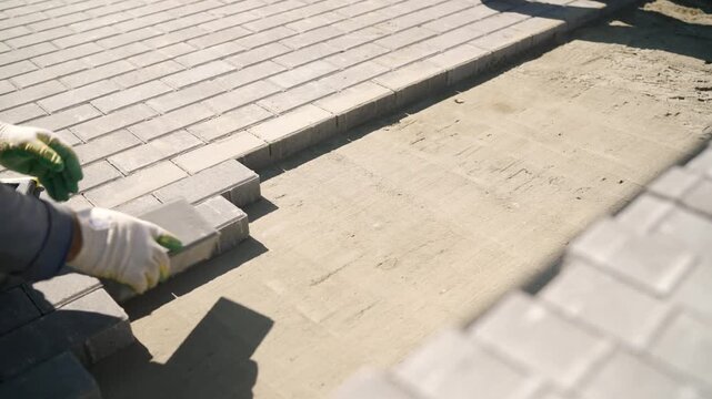 Laying gray interlocking brick pavers on a prepared sand base, creating a durable pavement for outdoor patio construction