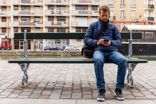 Vue de face d'un homme assis sur un banc en train de regarder son t&eacute;l&eacute;phone, Paris