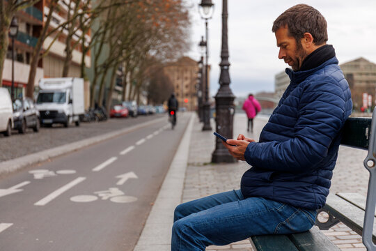 Un homme assis sur un banc en train de regarder son t&eacute;l&eacute;phone, Paris