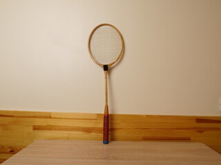 Old wooden sports racket leaning against a wall above a wooden surface.
