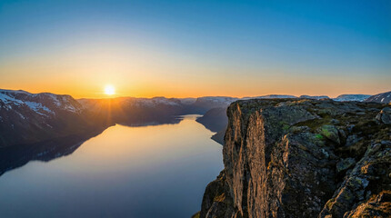 Majestic sunrise over a serene fjord surrounded by snow-capped mountains and rocky cliffs
