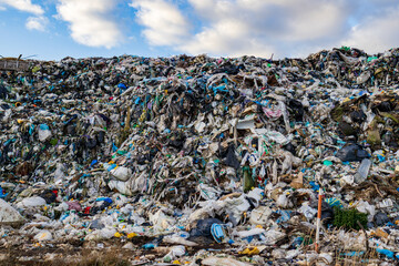 Large pile of garbage sits at a landfill site with plastic, food waste, and other rubbish strewn across the area as clouds gather overhead