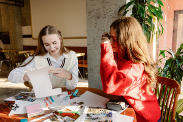 Two young women enjoy a fun afternoon in a cozy caf&eacute;, surrounded by colorful materials. They are engaged in a creative project, sharing laughter and ideas while making art.