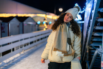 Fototapeta premium A young woman happily poses with her beanie pulled low, surrounded by shimmering holiday lights, embodying the joy of the winter season.