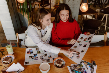 Fototapeta premium Two friends sit together at a wooden table, excitedly discussing photos and designs. They enjoy drinks while brainstorming ideas for a fun art project, surrounded by a warm ambiance.