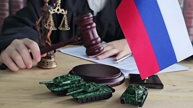 Court session with miniature tanks and Russian flag presented on the table during legal proceedings in a courtroom setting