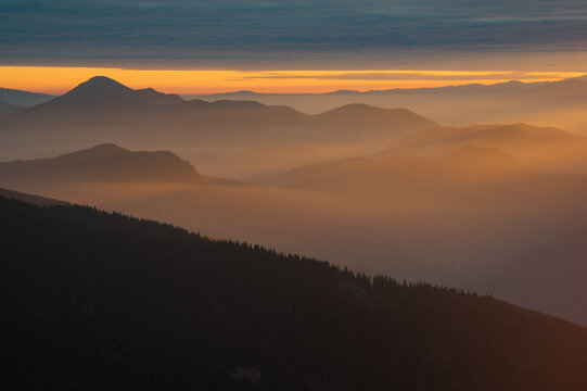 Aerial view of a serene landscape where layers of mountains fade into a golden mist beneath a soft dawn sky, Mala Fatra, Zilina Region, Slovakia.
