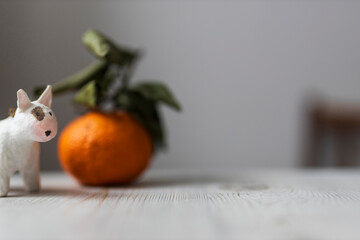 Small white dog figurine on table with fresh mandarin and green leaves blurred in background. Christmas card with copyspace