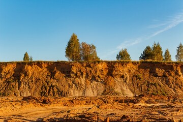 Sand quarry with a steep clay cliff under a clear blue sky, green trees on top