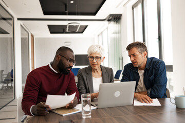 Business Meeting With Colleagues Reviewing Documents And Laptop In Modern Office