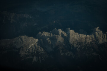 Aerial view of jagged, snow-dusted peaks pierce through the darkness, their rocky faces catching the light in a stark, dramatic contrast, Munich, Bavaria, Germany.
