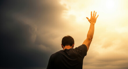 Rear view of a man raising his hand up to the sky with dramatic dark clouds and golden light, symbolizing hope and inspiration.