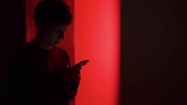 Man doomscrolling bad news on phone, standing in doorway with red light, anxiety and stress from constant negative information