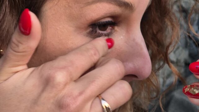 Woman eye cosmetics, applying eyeliner or adjusting lower lashes in extreme close up outdoors.