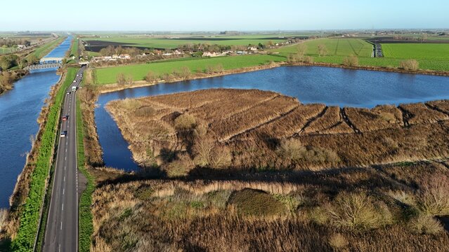 Aerial view of a serene landscape where a river flows beside a road near a tranquil lake, Ely, England, United Kingdom.