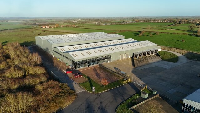 Aerial view of an industrial building with a large parking area and green fields stretching into the distance, Ely, England, United Kingdom.