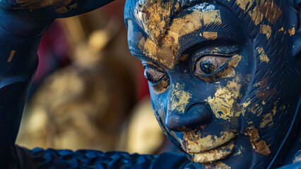 Close up of temple statue face covered in applied gold leaf from devotional prayers