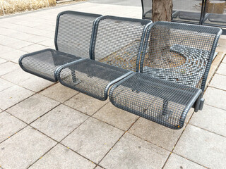 Urban metal mesh bench on pavement by tree in city park