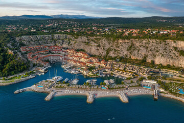 Aerial view of the harbor with boats nestled against the backdrop of towering cliffs and terracotta rooftops, Portopiccolo Sistiana, Friuli-Venezia Giulia, Italy.