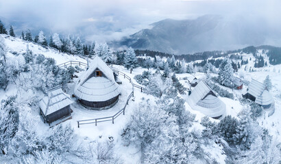 Naklejka premium High-resolution panoramic view of Velika Planina alpine village with traditional wooden shepherd huts in winter snow, Slovenia. aerial drone view