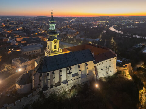 Aerial view of a medieval castle standing majestically against the fading twilight, its illuminated facade a beacon in the ancient city, Nitra, Nitriansky kraj, Slovakia.