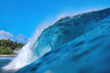 Powerful ocean wave curling under sky, palm silhouettes on horizon, translucent turquoise barrel breaking
