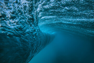 Underwater view breaking ocean wave tunnel deep blue barrel curling above, light filtering through translucent