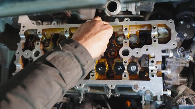 Mechanic installs hydraulic valve lifter into valve seat on internal combustion engine. Close-up of engine repair, parts replacement, maintenance. Process of overhauling engine block and cylinder head