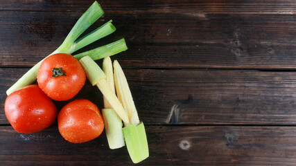 Top view fresh tomatoes, baby corn and leek on wooden board background with copy space for text