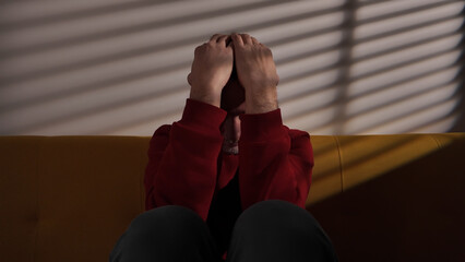 Man with headache, depression, sadness and loneliness sitting on a couch at home