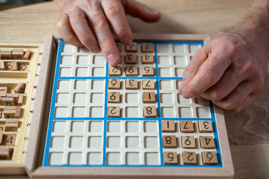 closeup hands carefully placing number into Sudoku puzzle, senior man focused on solving puzzle on wooden board, Brain exercise, cognitive health, and mental agility in mature age, brain health