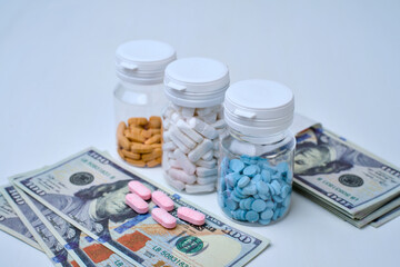 Assortment of prescription pill bottles and loose medication placed beside stacks of one hundred dollar bills.