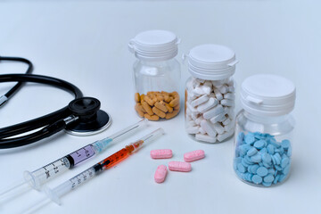 Medical supplies including a black stethoscope, syringes with liquid, and various colored prescription medication pills.