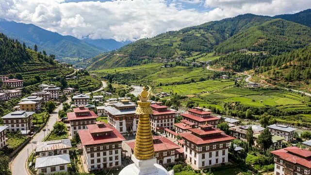 Panoramic aerial view of traditional Bhutanese architecture with white stupa and lush green mountain landscape under a partly cloudy sky