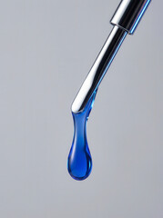 Close-up of a single blue liquid drop falling from a metallic dropper