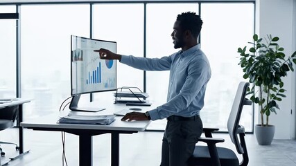 Focused businessman analyzes data and financial charts on a modern standing desk in a bright contemporary office with large windows overlooking a city view - Powered by Adobe