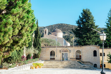 Ancient stone church complex surrounded by trees and mountains under clear blue sky. Saint Neophytos Monastery in Cyprus