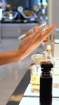 Woman's hand selecting and testing a new fragrance from a beautifully displayed collection in a cosmetic store, showing the elegant bottle and the blurred background of a luxury shop