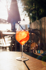 Orange cocktail in wine glass on outdoor cafe table with sunlight and seaside background. Closeup