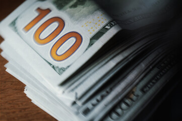 A pile of paper money: American dollars in denominations of $100 and $100 bills. A stack of crumpled bills on a wooden oak table, close-up, blurred, with selective focus.