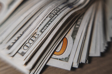 A pile of paper money: American dollars in denominations of $100 and $100 bills. A stack of crumpled bills on a wooden oak table, close-up, blurred, with selective focus.
